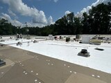Flat low-slope commercial roof with white single-ply membrane rolled over mechanically fastened cover board, drains and curbs across the deck