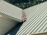 Finished green standing-seam metal roof, two pitched panel planes meeting at the valley above a white gutter line
