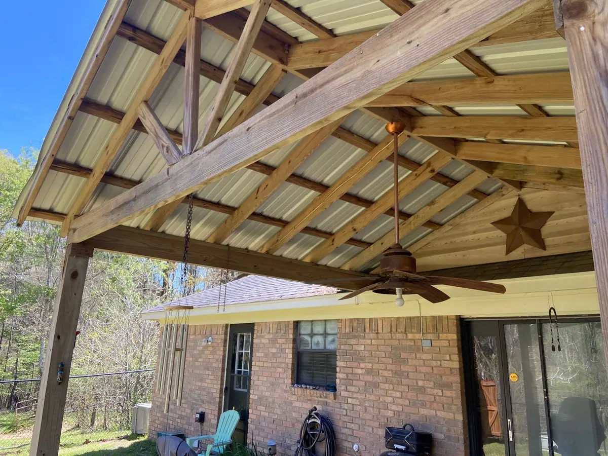 Timber-framed patio cover with a metal roof and a ceiling fan over a brick home, outdoor living