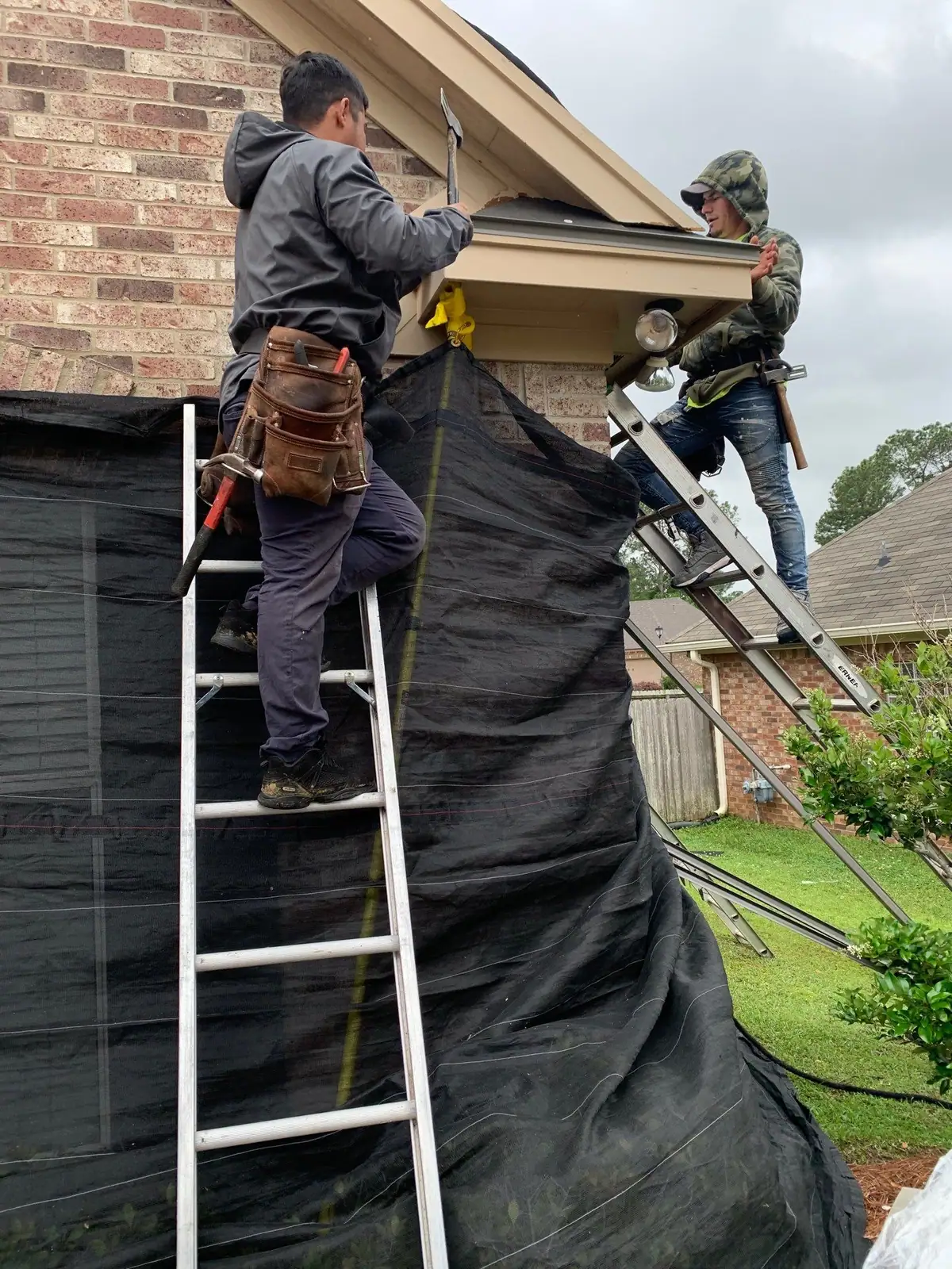 Two workers on ladders repairing the fascia and soffit at a gable eave