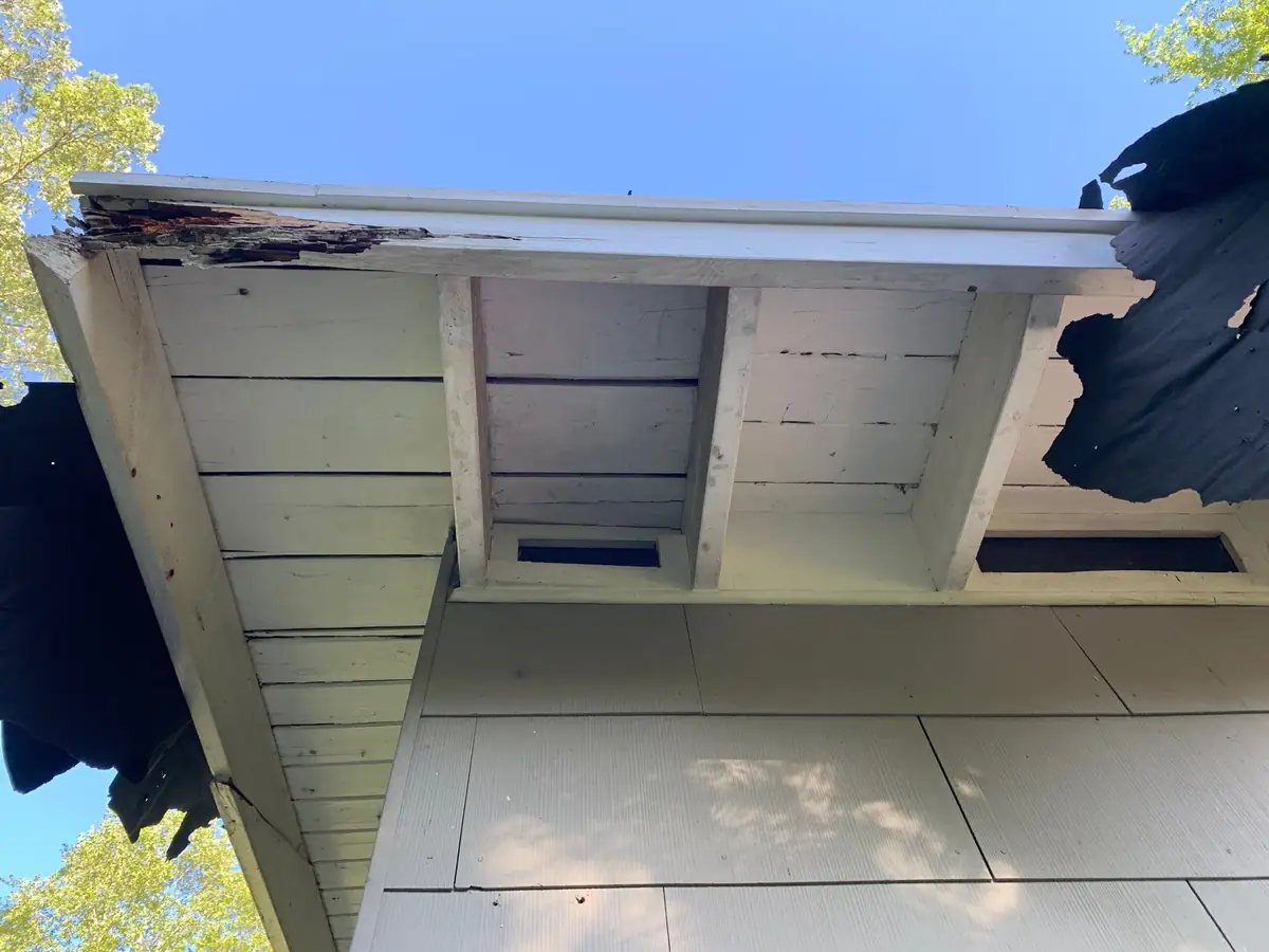 Rotted fascia corner and loose soffit panels on a house