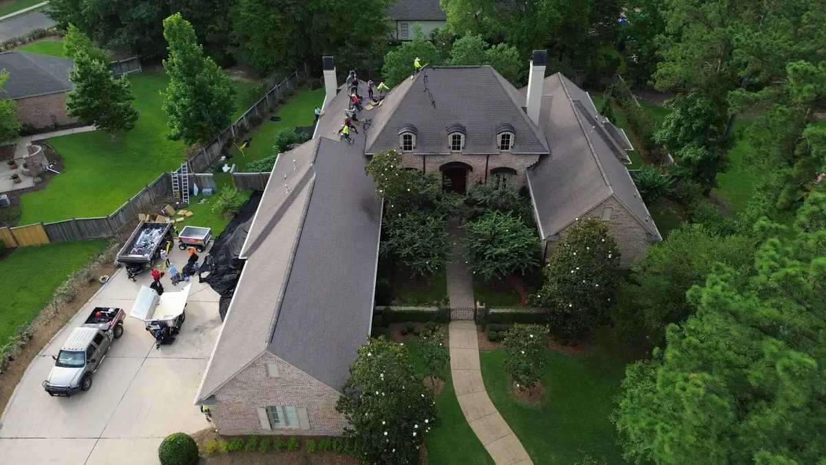 Large brick home with a new roof, crew trucks in the drive, from above