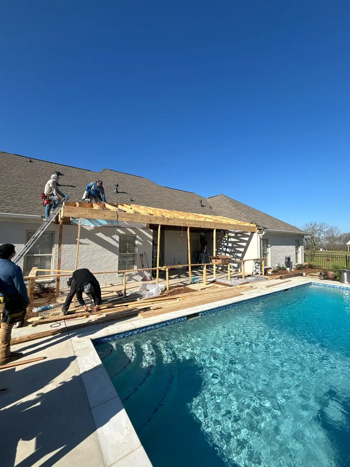 Crew framing a covered patio roof beside a backyard pool for outdoor living