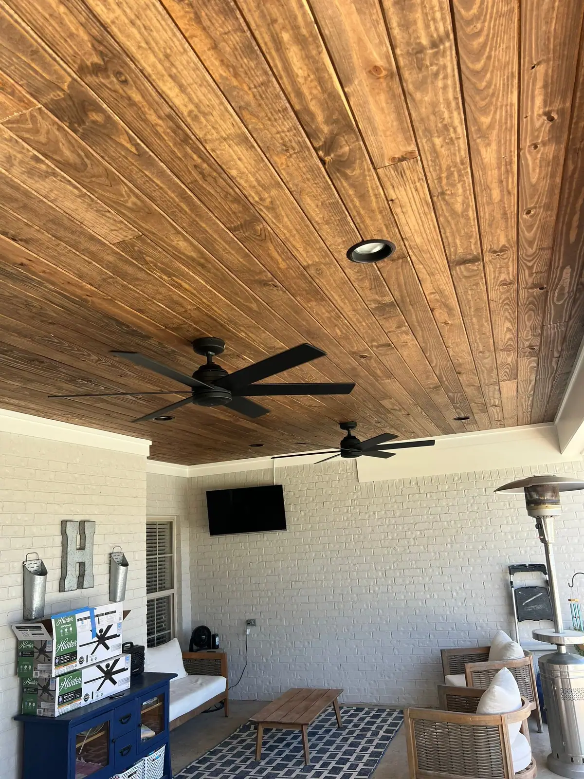 Finished covered patio with a stained wood ceiling, ceiling fans and a TV wall, an outdoor living space