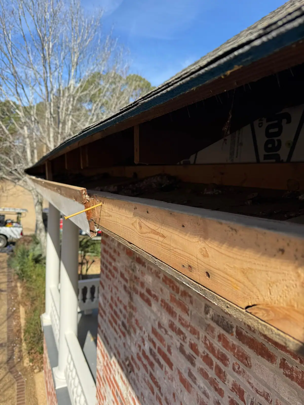 Bare fascia board along a brick wall with the gutter removed