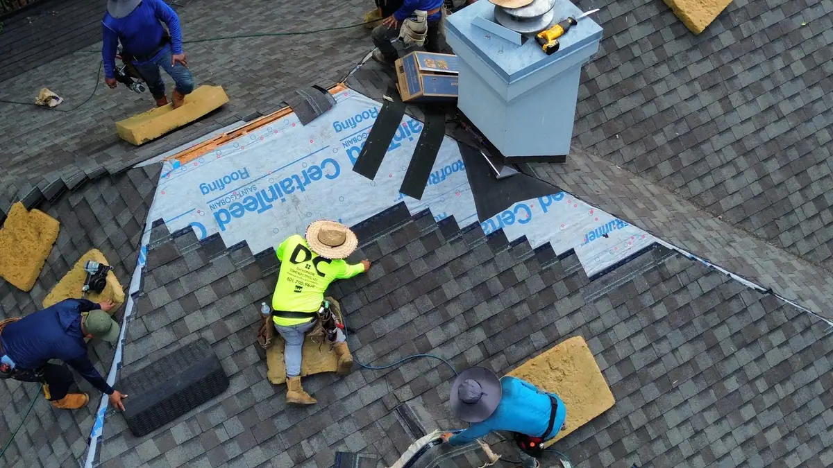 Roofers installing shingles around a chimney on a Dickerson Contracting roofing job, seen from above