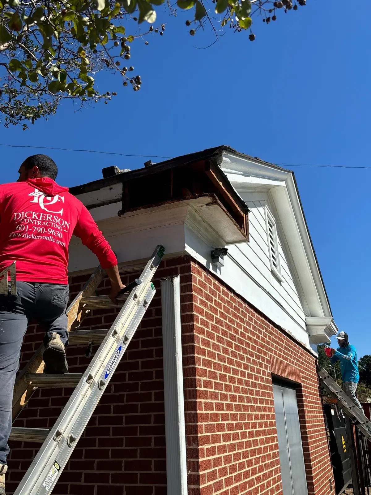 Worker climbing to an opened cornice on a brick building for fascia and soffit repair