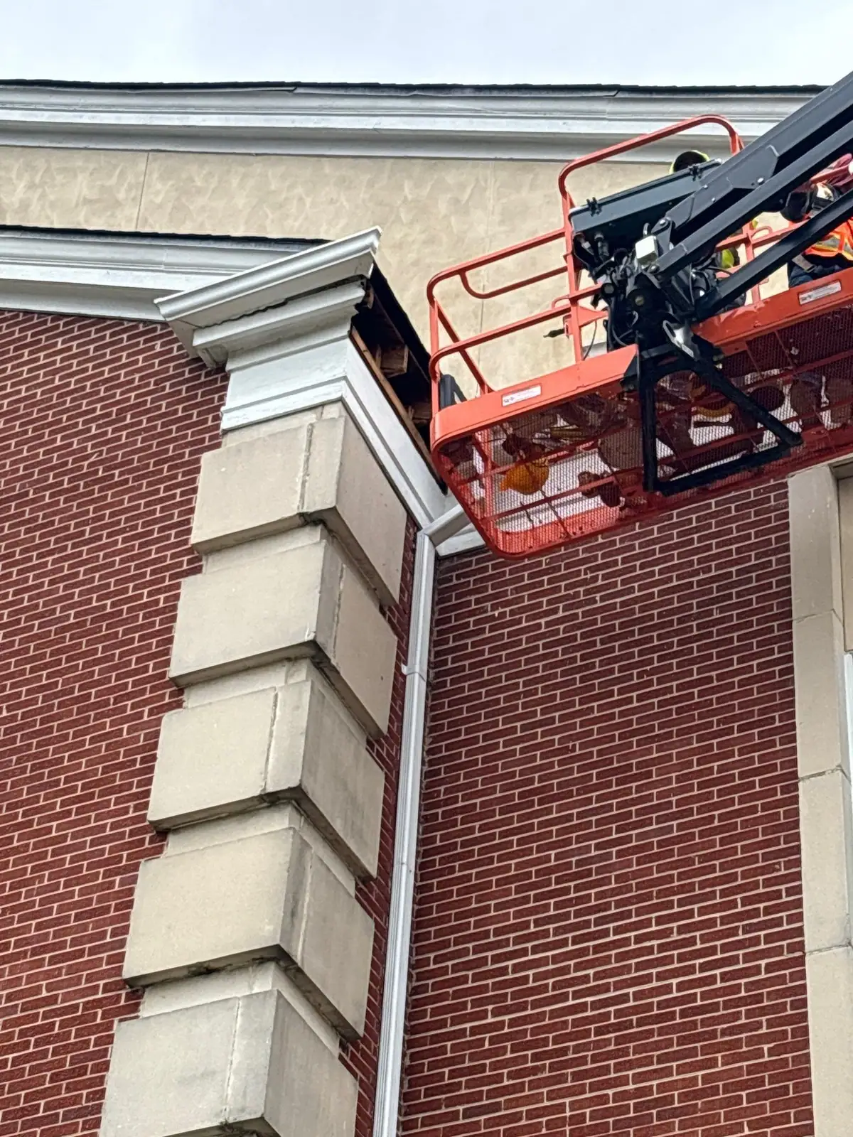 Crew working from a lift on fascia and soffit repair at the cornice of a tall brick building