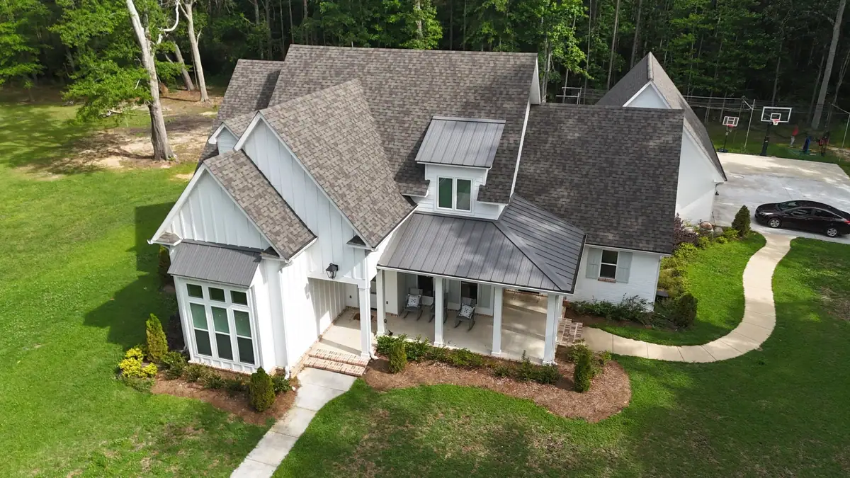 White farmhouse with a new shingle roof and standing seam porch accents by roofing company Dickerson Contracting