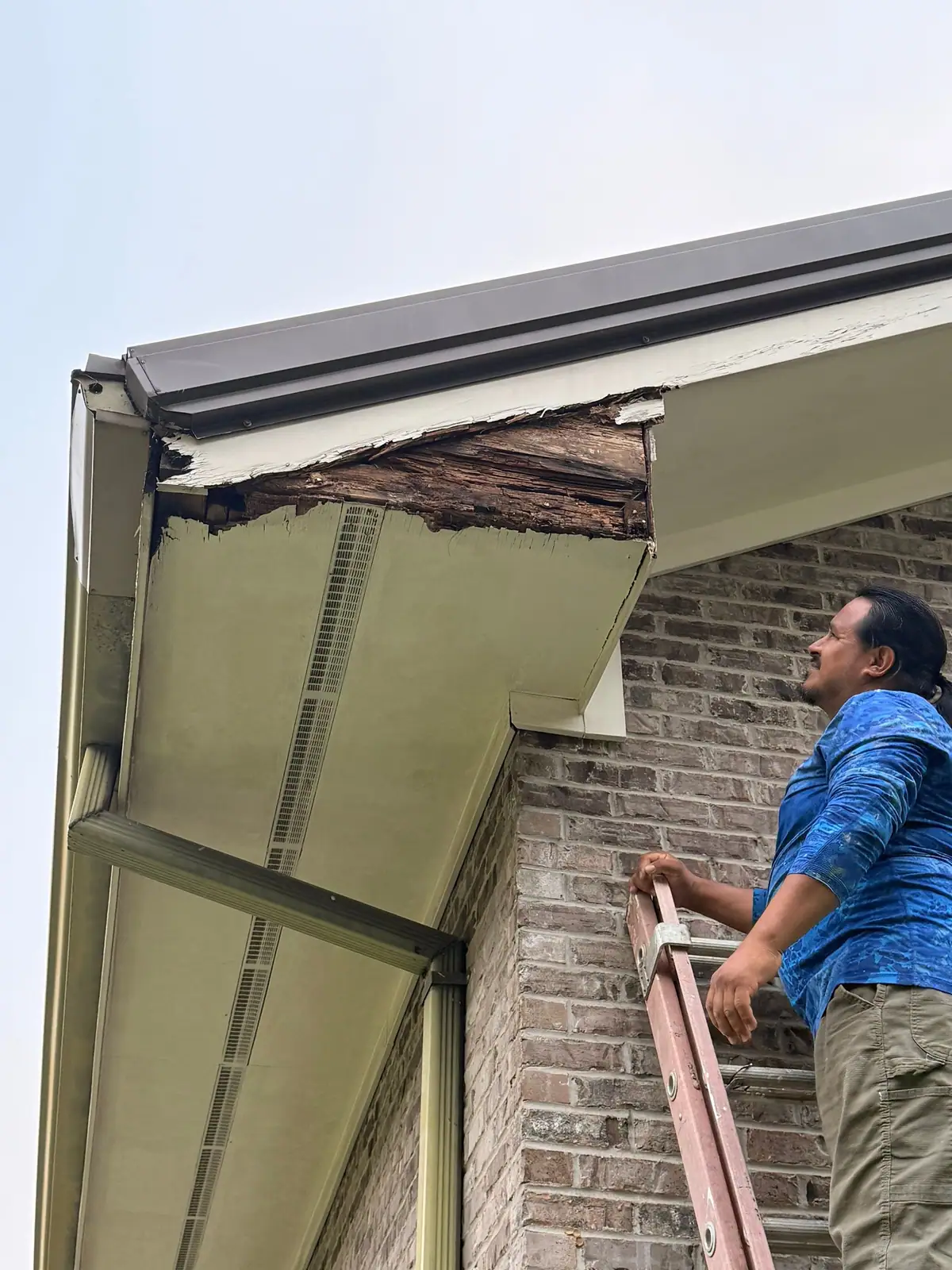 Worker on a ladder checking a rotted soffit corner before soffit repair