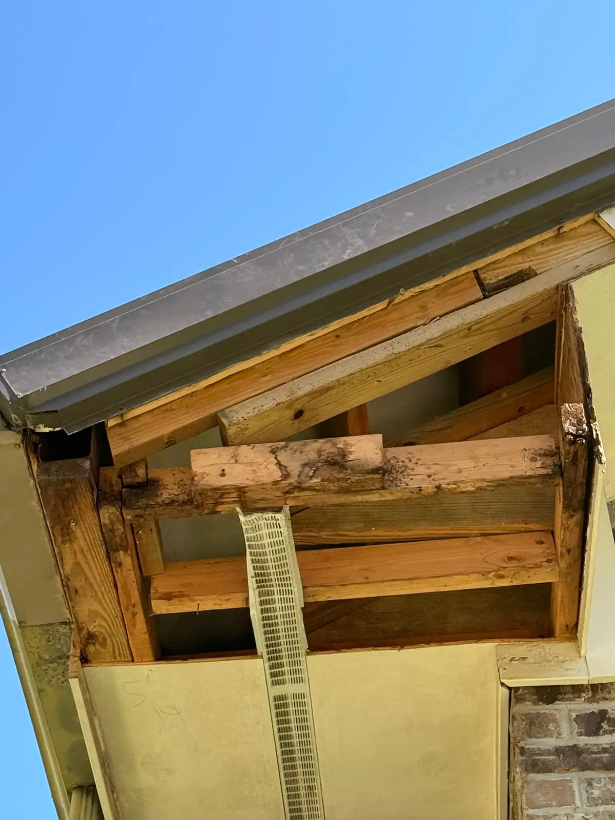 Rotted lookouts and fascia framing exposed under a church eave