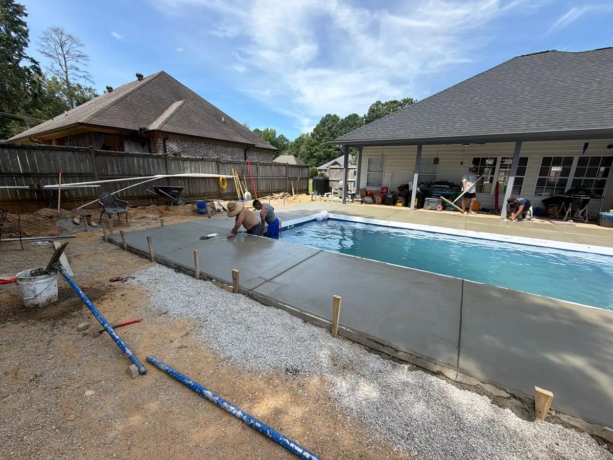 Crew finishing the concrete deck around a new fiberglass pool by DC Pools and Spas, pool company serving Clinton, MS
