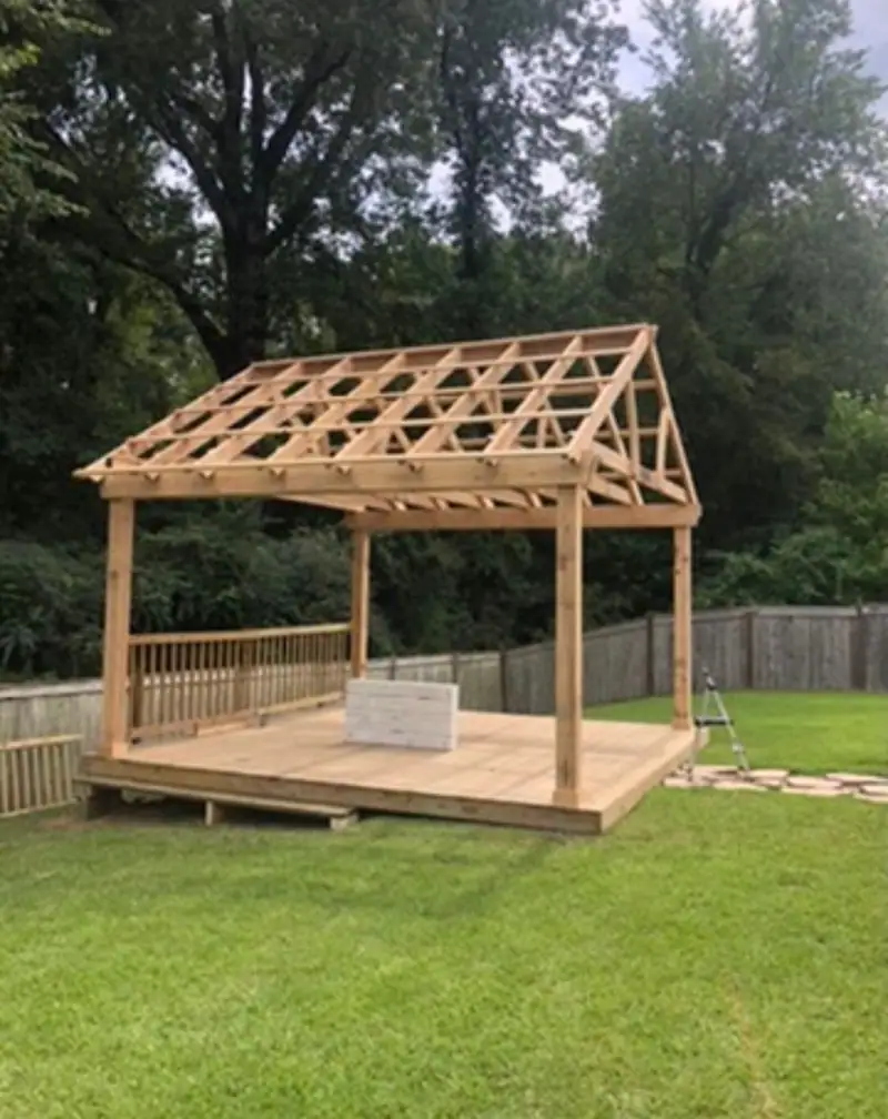 Pavilion framing going up on a new wood deck, an outdoor living build in a fenced backyard
