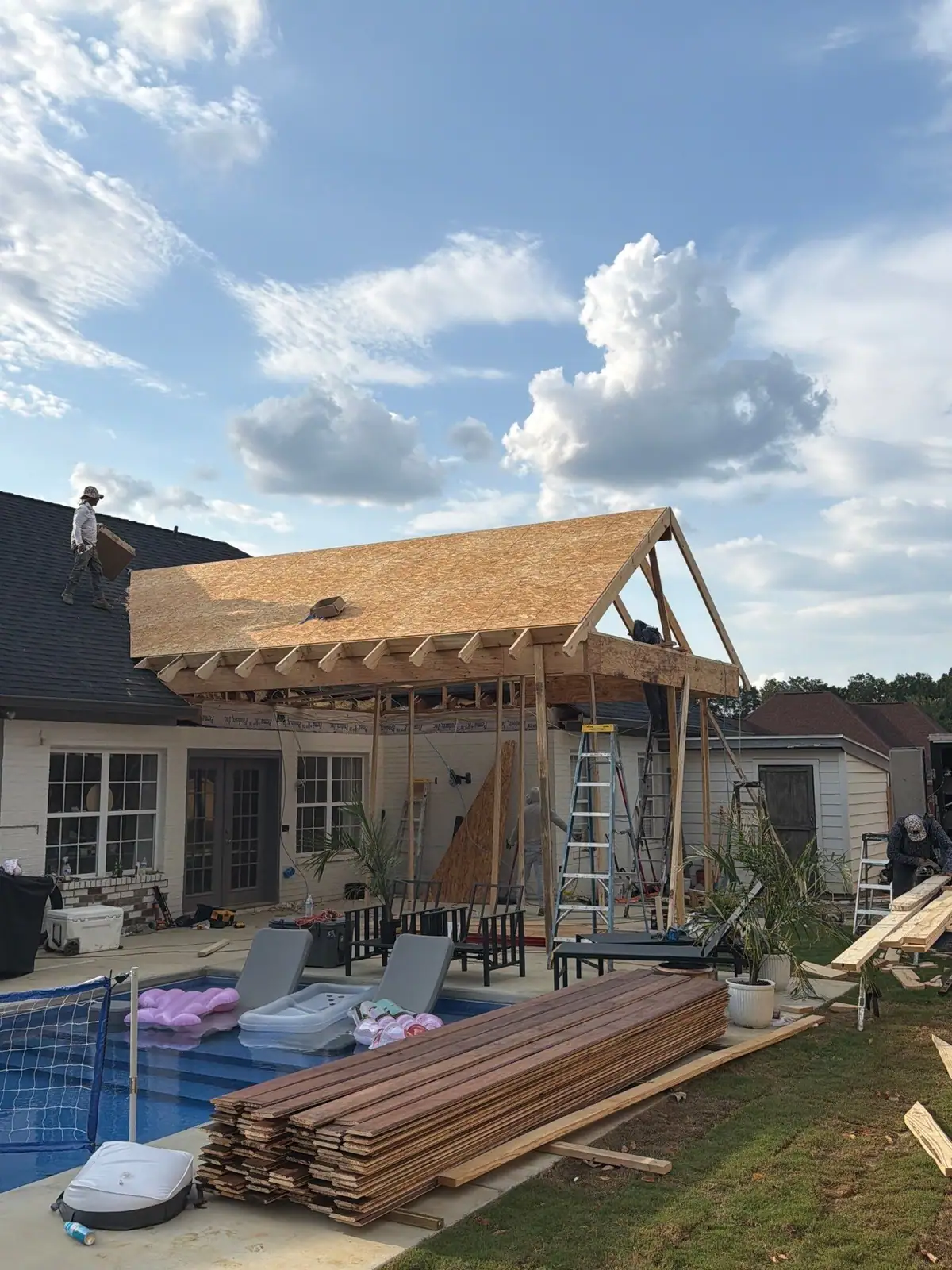 Crew decking the gable roof of a poolside pavilion built over an outdoor kitchen