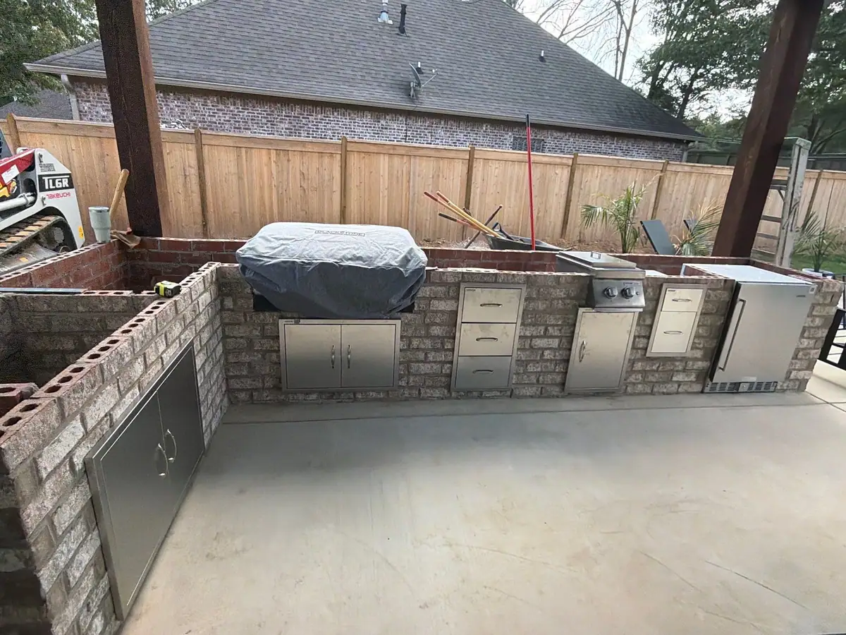 Brick outdoor kitchen under a covered pavilion with a built-in grill, drawers and refrigerator