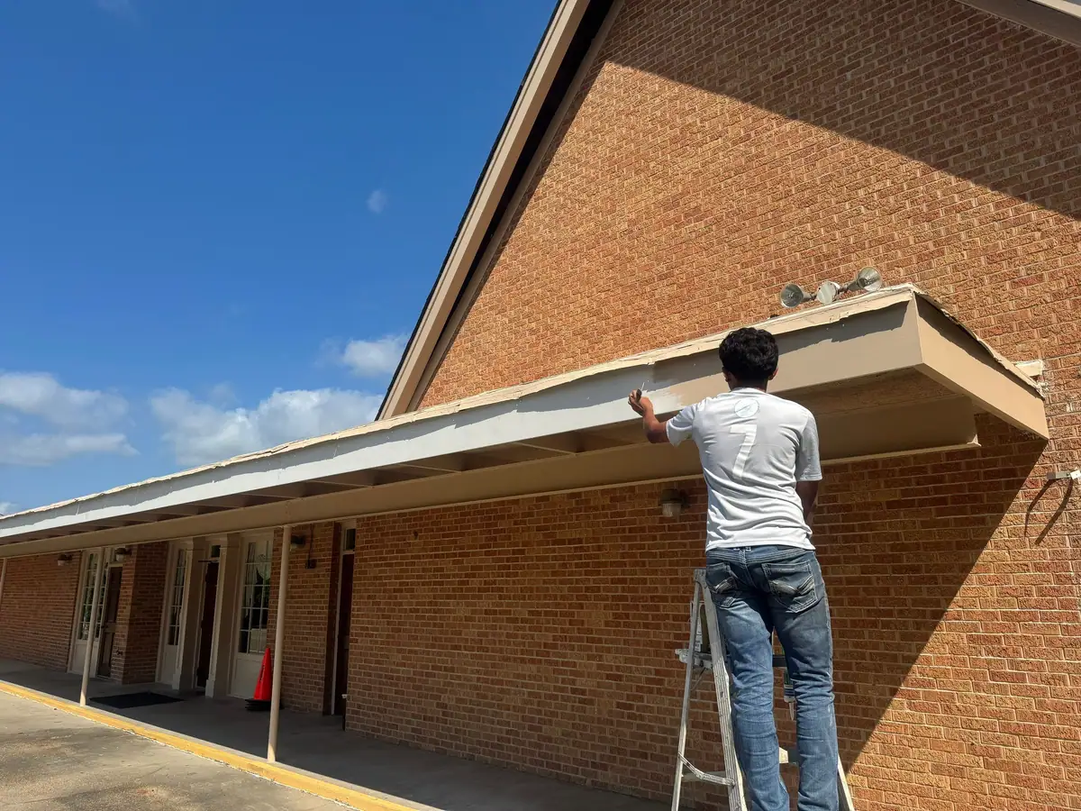 Worker on a ladder repairing a canopy fascia on a Dickerson Contracting job