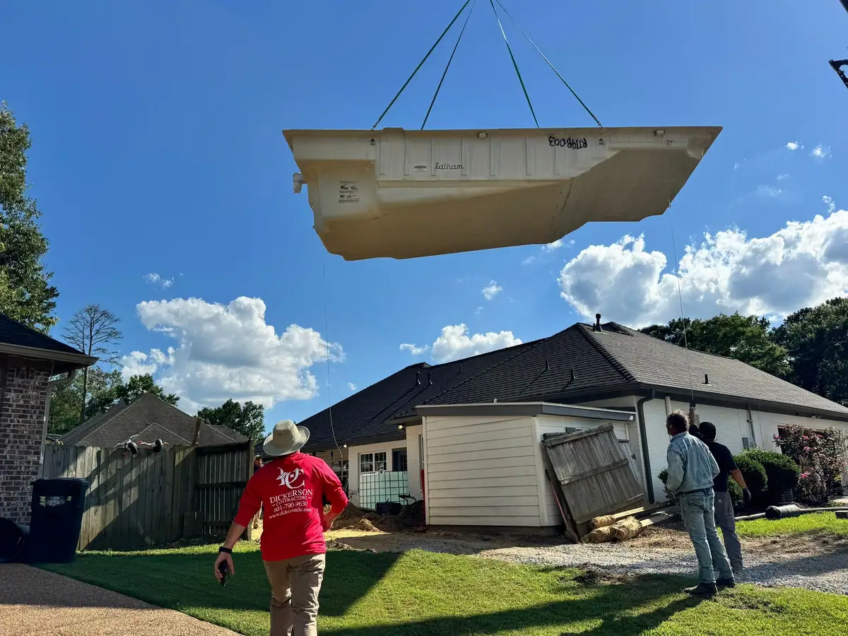 Crane lowering a one-piece fiberglass pool into a backyard, pool company DC Pools and Spas serving Jackson, MS