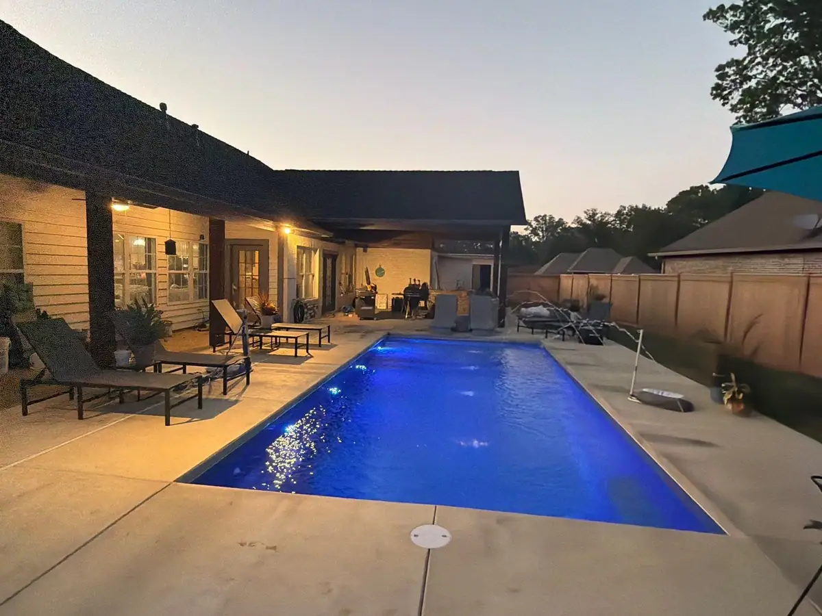 Finished fiberglass pool lit at dusk beside a covered patio, pool company DC Pools and Spas serving Jackson, MS