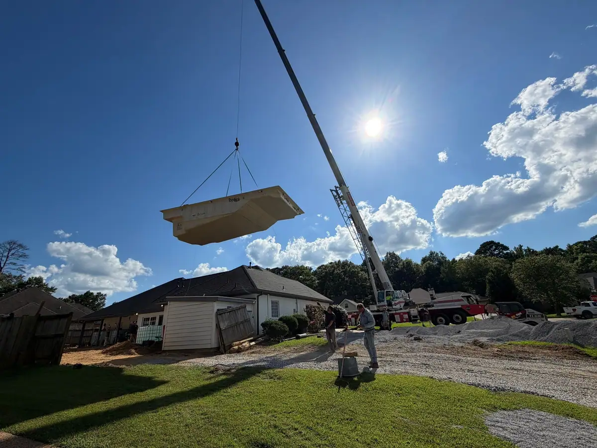 One-piece fiberglass pool shell held by a crane before setting, serving Madison, MS