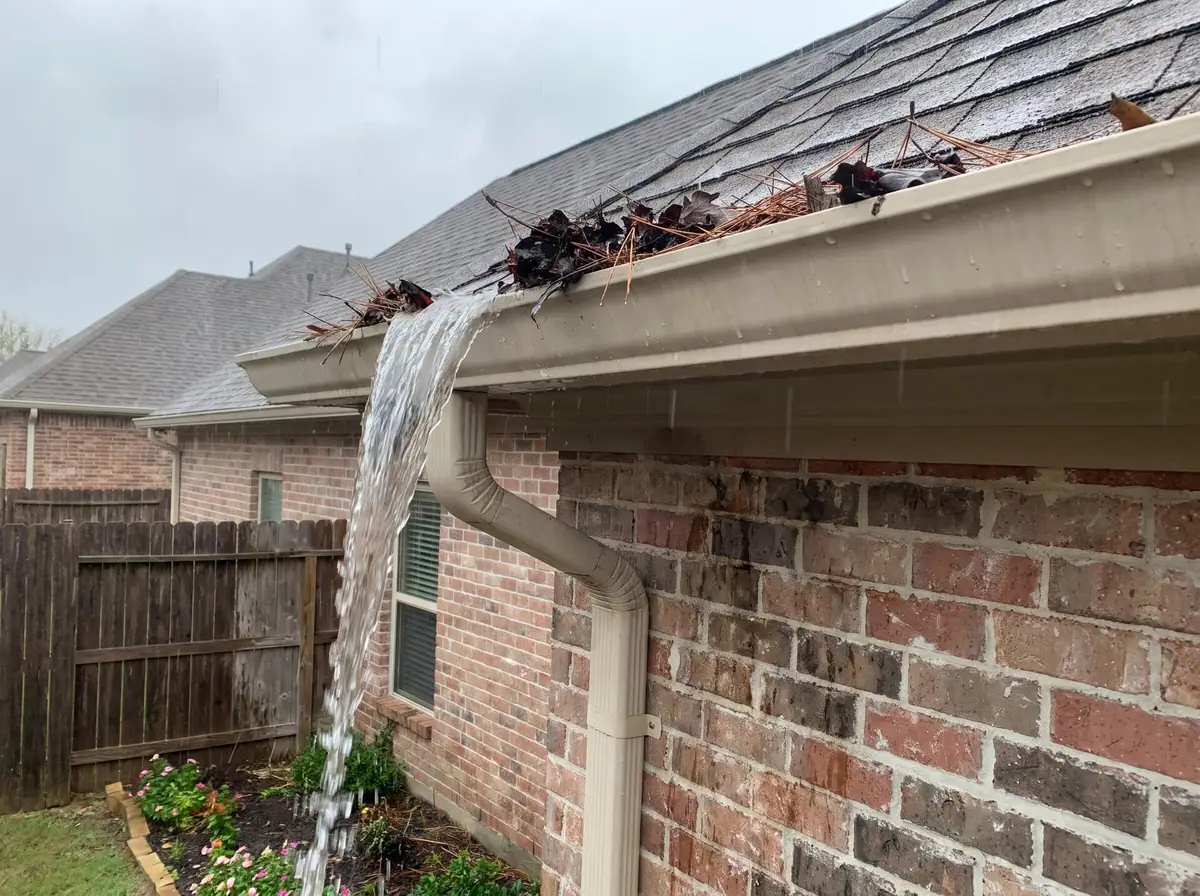 Gutter clogged with leaves overflowing over the front edge in the rain