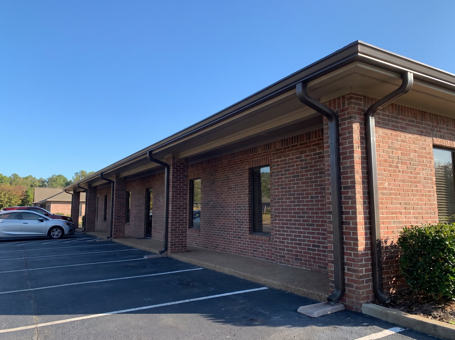 Dark gutters and downspouts along a single-story brick office building, commercial gutter installation