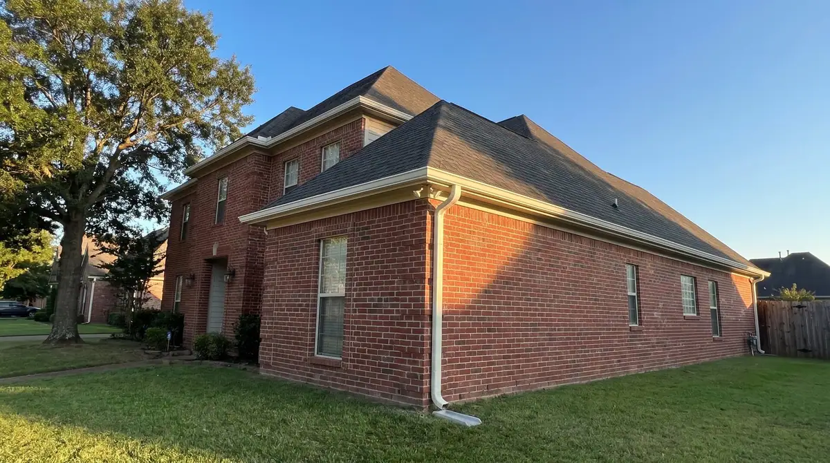 Gutter installation illustration: white seamless K-style gutters and downspout on a two-story red brick home